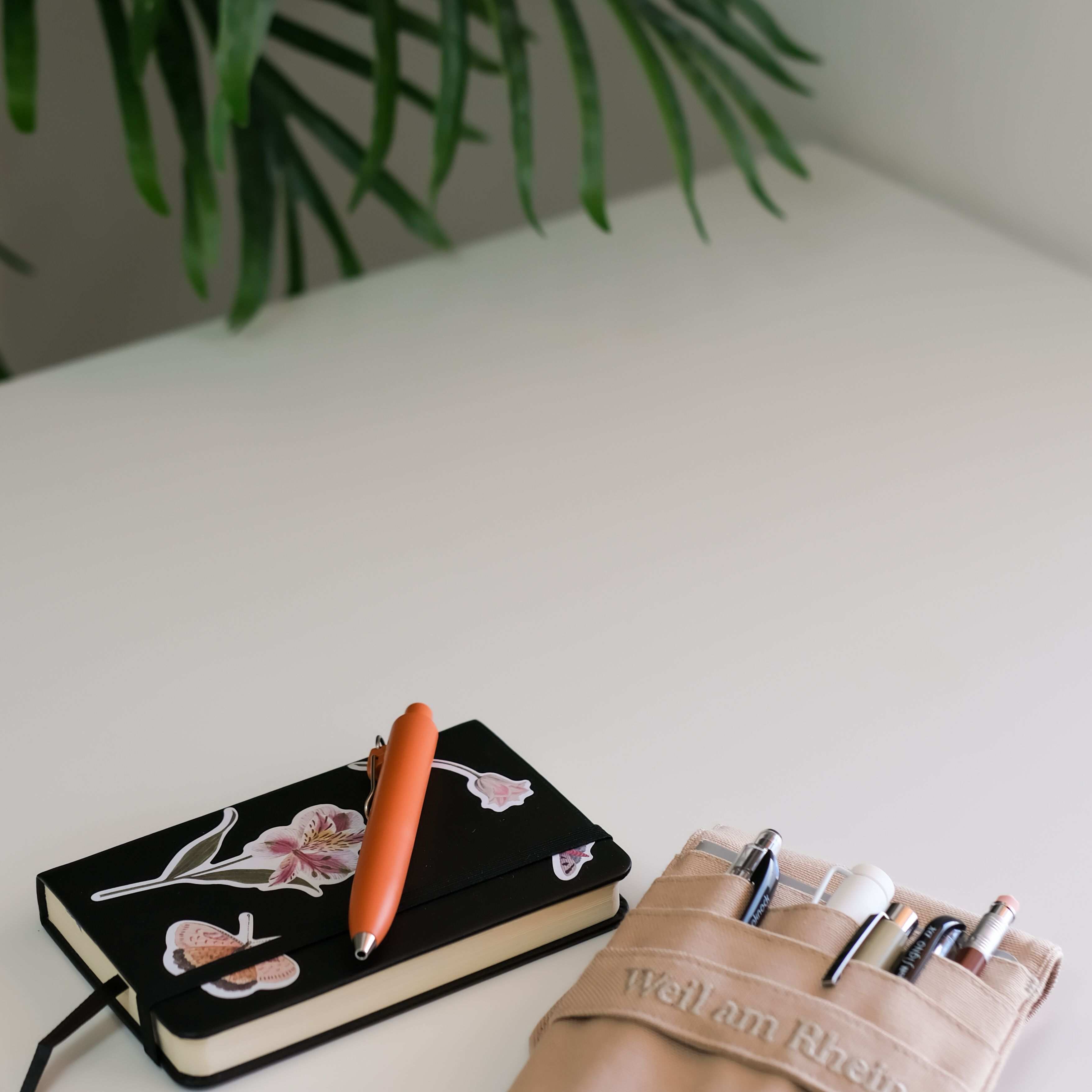 Minimalistischer Arbeitsplatz mit Notizbuch und Stiften auf weißem Schreibtisch